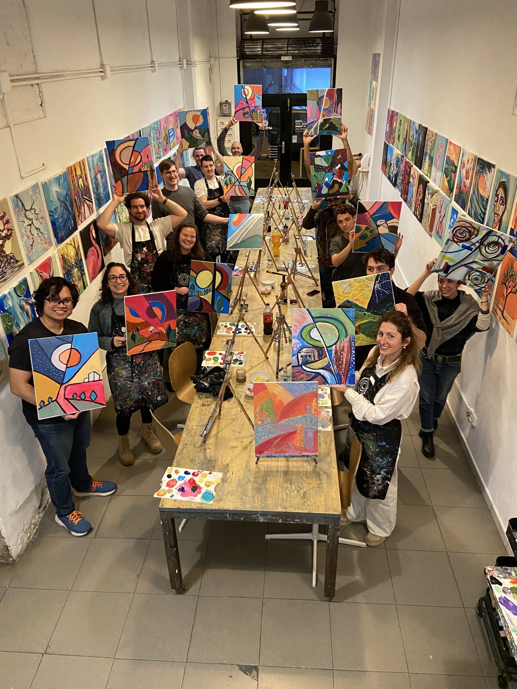 The team holding up their canvases at a painting class