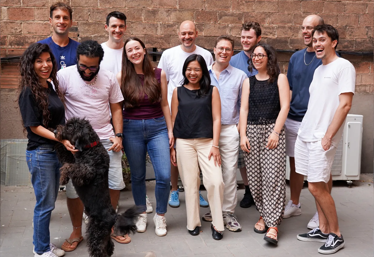 The Noloco team together in a courtyard, with a black dog jumping up to greet them
