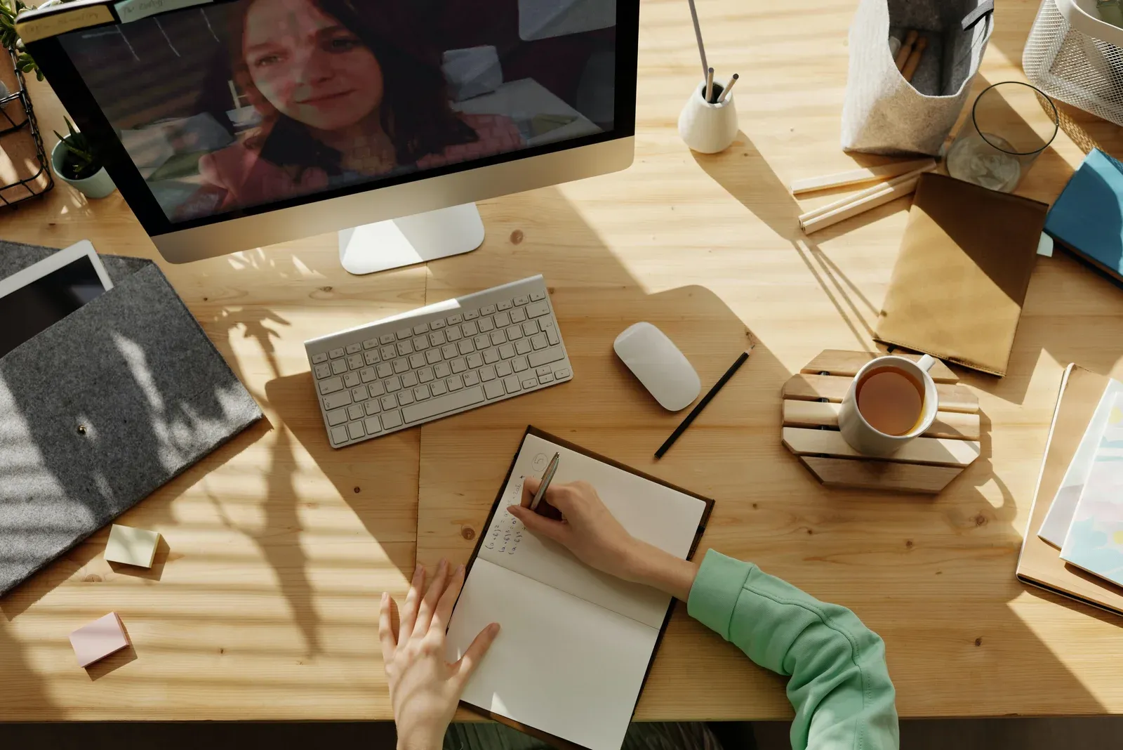 A person writing in a notebook at a desk during a video call
